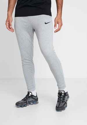 Szare sportowe spodnie o wąskim kroju, z czarnym logo Nike na udzie. Noszone z czarnymi butami do biegania i białymi skarpetkami.