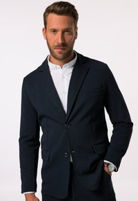 Maßgeschneiderter dunkelblauer Blazer aus weichem Stoff, mit Ein-Knopf-Verschluss, Reverskragen und zwei vorderen Taschen. Trägt man über einem weißen Hemd.