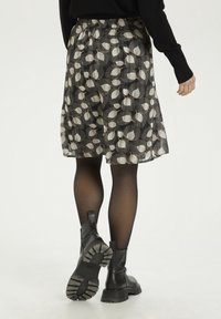 Jupe noire à fleurs, longueur aux genoux, motifs de feuilles blanches, ceinture élastique, tissu transparent, portée avec des bottines noires et des collants.