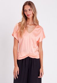 Haut pêche à col en V avec des manches courtes, détail noué à la taille, fabriqué en tissu léger et brillant. Associé à un pantalon noir ample.
