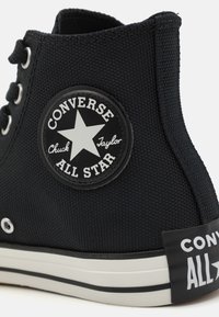 Zapatillas altas de lona negra con una superficie texturizada, suela de goma blanca y un notable parche de logo circular con una estrella.