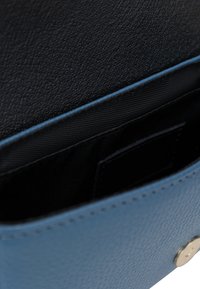 Interno di un portafoglio in pelle blu testurizzata con una fodera nera liscia, dotato di uno scomparto per carte piccolo e un dettaglio hardware rotondo dorato.