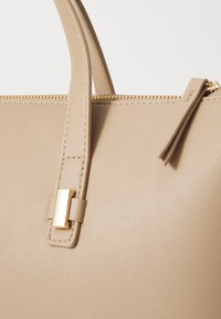 Beige leather handbag with smooth texture, featuring a gold-tone hardware accent and sturdy handles. Zipper closure visible at the top.