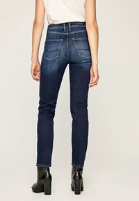 Mörkblå denim skinny jeans med medelhög midja, två bakfickor och en mjuk textur, matchat med svarta klackiga ankelstövlar.