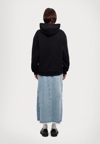 Felpa nera con cappuccio e vestibilità ampia, indossata con una lunga gonna di jeans azzurri e scarpe con plateau nere. La gonna ha orli sfrangiati.