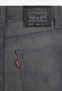 Grå denim Levi's 511 jeans med svart etikett, rød tab, og distinkte baklommestikking detaljer. Har fem lommer og beltehemper.