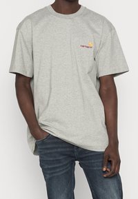 Szary t-shirt z krótkim rękawem, wykonany z mieszanki bawełny, z okrągłym dekoltem. Posiada małe logo Carhartt na lewej piersi. Luźny krój.
