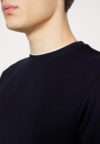 Pull marin à col rond avec une texture douce, présentant un détail contrastant à l'intérieur du col. Le tissu apparaît lisse avec des coutures minimales.