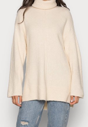 Maglione a collo alto color crema realizzato in un morbido tessuto testurizzato, con maniche ampie e orlo a costine, dal taglio relaxed.