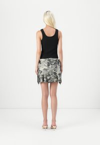 Svart tank topp parret med et mini-skjørt i camo-mønster som har plisse-design og rå kant. Lys fargeskjema med nøytrale sandaler.
