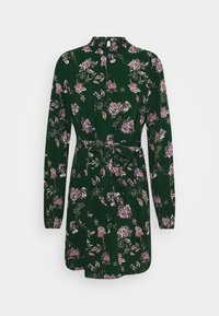 Robe florale verte à manches longues, taille cintrée et ceinture nouée. Présente des fleurs roses et blanches sur un tissu texturé. Fermeture par boutons dans le dos.