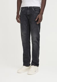 Jeans de mezclilla oscura con corte recto, con cierre frontal de botón y cremallera, y bolsillos laterales. Combinados con zapatillas deportivas blancas.