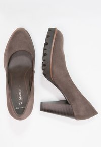 Zapatos de tacón alto de ante marrón con una puntera amplia, tacón de bloque texturizado y diseño minimalista. La plantilla presenta un sutil logotipo y la talla.