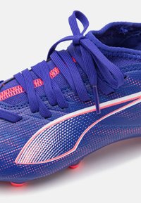Crampon de football violet avec des accents roses, tige texturée et design à rayures diagonales. Comprend des lacets et un col doux. Conçu pour la performance.