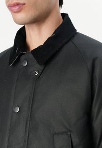 Veste noire avec un col en velours côtelé, boutons pression et une texture lisse. Comprend une poche avant et un design structuré.