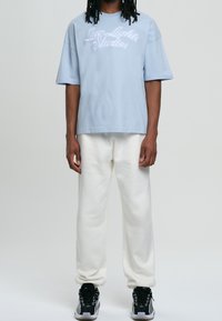 Ljusblå bomullströja med broderad text "Low Lights Studios"; kombineras med löst sittande vita sweatshirts och flerfärgade sneakers.