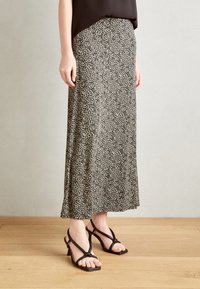Falda maxi de patrón en negro y crema, hecha de tela ligera, con un diseño fluido y una abertura lateral, combinada con sandalias negras de tiras.