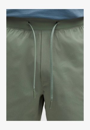 Nærbillede af grønne bukser med snøre og blød stoftekstur samt en synlig linning under en blå top.