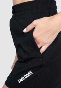Black shorts made of soft fabric, featuring a zippered pocket and elastic waistband. Logo "SMILODOX" displayed on the lower left side.
