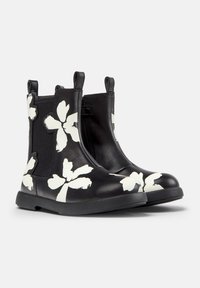Bottes noires à chevilles avec des motifs floraux blancs, des panneaux latéraux élastiques et des languettes de tirage sur un fond clair.