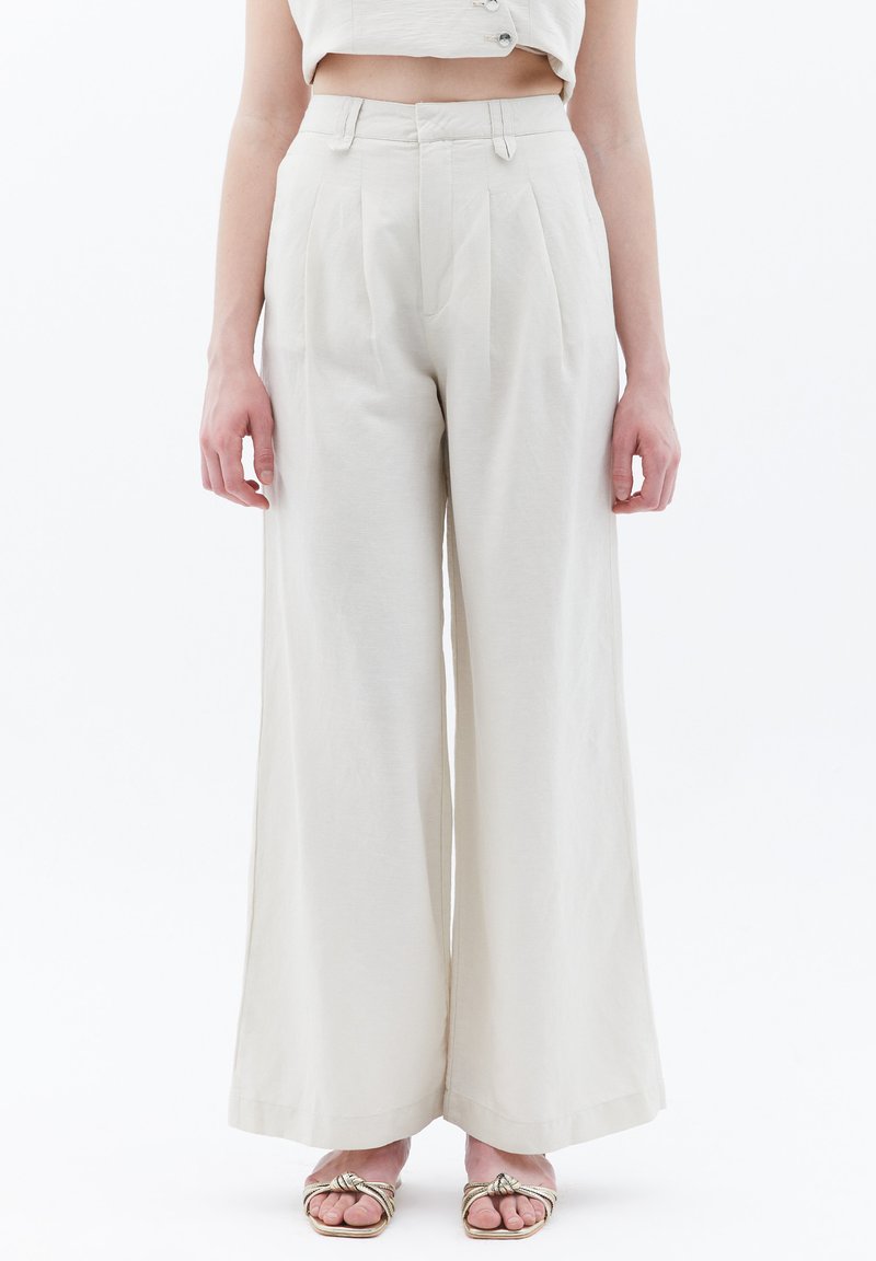 Ljust beiga vida byxor med framfickor, hög midja och en slät, strukturerad tyg. Stylat med sandaler med remmar.