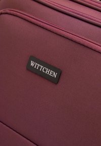 Borsa da viaggio bordeaux con tessuto testurizzato, dotata di una placca con logo "WITTCHEN" nera e compartimenti con doppio zip. Design compatto.