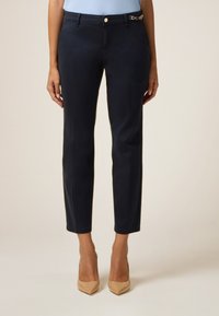 Pantalons taillés bleu marine avec une coupe slim, présentant un accent décoratif doré sur la taille et une texture de tissu lisse.