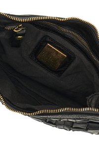 Interno di una borsa in pelle nera con cerniera dorata, foderato in tessuto e un piccolo cartellino metallico che indica il marchio. Texture liscia con un design elegante.