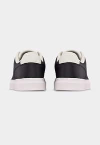 Paire de baskets basses noires et blanches vues de dos avec des semelles blanches sur un fond uni.