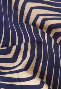 Tessuto blu navy e beige con un motivo a strisce a zigzag. La consistenza è liscia con un leggero rilievo sulla superficie.