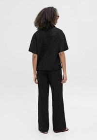 Ensemble en tissu noir à œillets comprenant un haut et un pantalon, avec une coupe ample et des manches courtes, orné de motifs floraux découpés et de jambes droites.