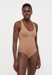 Beige shapewear bodysuit met een diepe V-hals, brede banden, een gladde textuur en een getailleerde silhouet. Geen zichtbare patronen of hardware.