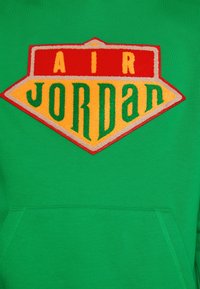 Sudadera verde con un gran logotipo "AIR JORDAN" colorido en rojo, amarillo y verde, con un diseño en forma de diamante y tela texturizada.