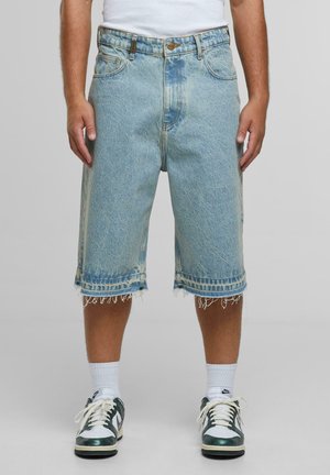 Lichtblauwe denim shorts met een rafelige zoom, vijf zakken en een knoopsluiting, gecombineerd met witte sokken en groene sneakers.