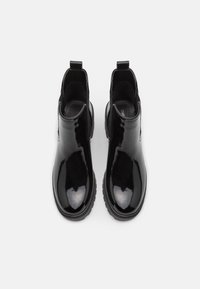 Botines de charol negro con paneles laterales elásticos y una tirador, que presentan una suela texturizada gruesa y un acabado suave.