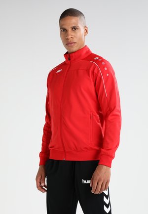 Giacca sportiva rossa con colletto alto, chiusura con zip, tasche laterali, dettagli bianchi e logo sul petto e sulla spalla.
