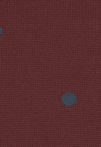 Un tissu maroon texturé présentant des pois bleus irréguliers dispersés sur la surface, créant un motif simple et moderne.