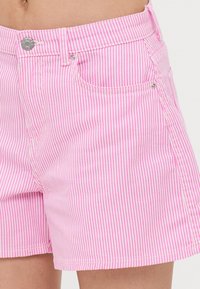 Pantalones cortos a rayas rosas de algodón, con un corte clásico, bolsillo delantero y un detalle de metal plateado en la cinturilla.