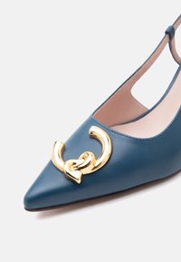 Chaussure slingback en cuir bleu à bout pointu, ornée d'une chaîne décorative dorée en maillons sur le devant.
