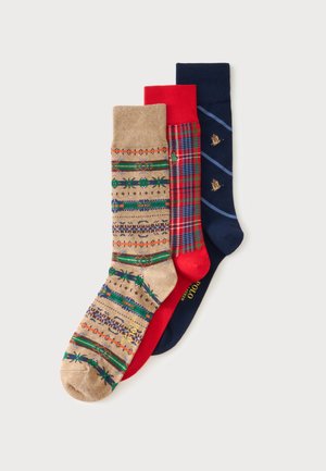 Trois chaussettes plates à motifs : beige avec des rayures géométriques, rouge avec un motif à carreaux, et bleu marine avec des rayures diagonales et petits motifs.