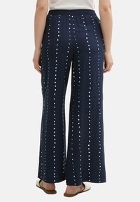 Navy wide-leg trousers with white polka dot pattern, elastic waistband, and soft fabric, styled with sandals. View from the back.