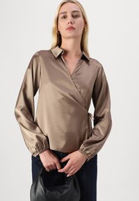 Camisa de manga longa em satin castanho claro, com gola e punhos elásticos, usada com uma bolsa preta.