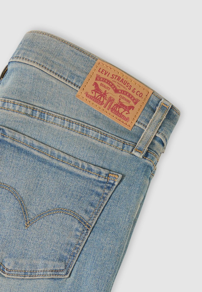 Lyseblå denimjeans, der viser baglommen og det brune Levi Strauss & Co. lædermærke med to heste-logo og syningsdetaljer.