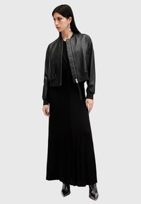 Chaqueta bomber negra de cuero con puños acanalados, llevada sobre un vestido maxi negro, acompañada de botas metálicas hasta el tobillo. Sencillos acentos de joyería de plata.