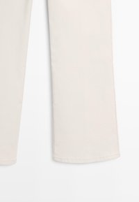 Unterer Teil von cremefarbenen Hosen mit weitem Bein und sichtbarer Naht am Saum vor weißem Hintergrund.