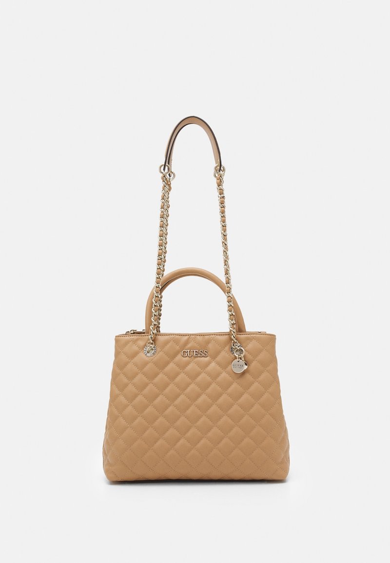 Sac à main matelassé beige avec chaîne dorée et bandoulière en cuir, poignées supérieures, et logo GUESS argenté avec pendentif sur le devant.