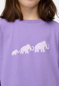 Lila Kurzarmshirt mit einem weißen Grafikdruck von drei Mammuts in einer Reihe, wobei das kleinste links und das größte rechts ist.