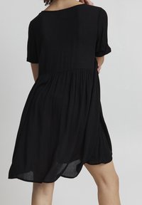 Svart klänning med lös passform, korta ärmar och definierad midja. Tillverkad av lätt, texturerad tyg med en utfälld kjol.