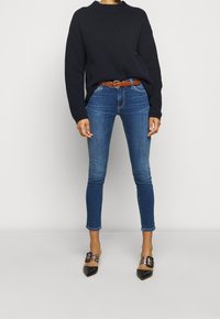 Marinblå stickad tröja, åtsittande blå denimjeans, brun bälte och svarta klackskor med spetsig tå och dekorativa detaljer.