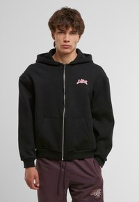 Felpa nera con zip realizzata in un mix di cotone, con una grande tasca frontale e un logo rosa sul lato sinistro del petto. Il design include un cappuccio con stringhe.